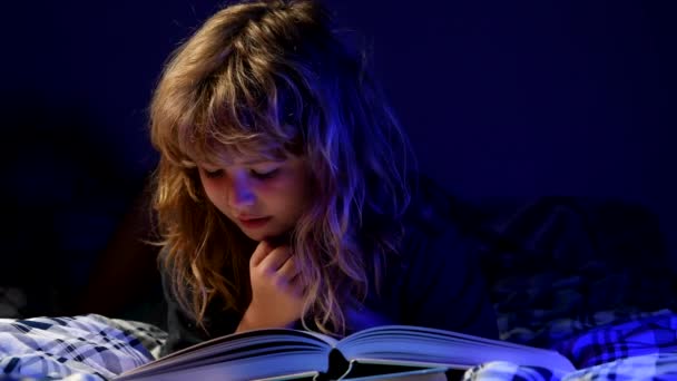 Niño pequeño leyendo un libro en la casa oscura. Cara de niños con luz nocturna. — Vídeo de stock