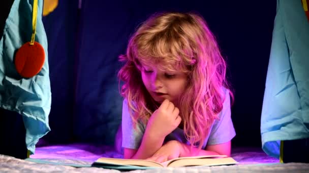 Niño leyendo un libro en la casa oscura. Niño serio leyendo libros, se ve serio y concentrado, jugando en casa, lee cuentos o cuentos de hadas. — Vídeo de stock