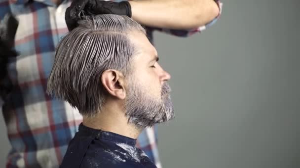 Facet z brodą farbuje włosy. Fryzjer, farbowanie włosów. Atrakcyjny starszy fryzjer robi fryzurę i kolor włosów dla klienta w salonie fryzjerskim. — Wideo stockowe