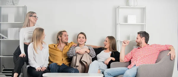 Gruppo di giovani seduti sul divano e che parlano a casa. Giovani amici che si divertono in salotto. — Foto Stock
