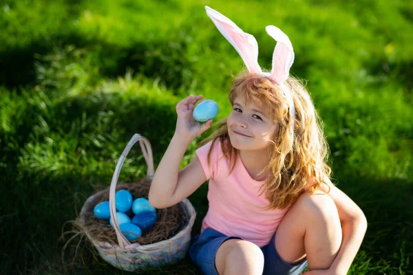 Wielkanocny króliczek. Dziecko w króliczych uszach polujące na wielkanocne jajka na podwórku. Polowanie na pisanki. — Zdjęcie stockowe