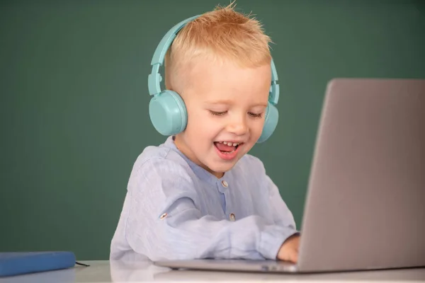Menino feliz em fones de ouvido usando um laptop e estudar on-line com professor de videochamada na escola. Estudo remoto e educação. — Fotografia de Stock