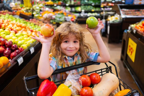 Bambino che sceglie una mela in un negozio. Divertente bambino sorridere e tenere la mela. Un ragazzo che fa shopping al supermercato. Ragazzino che sceglie mela fresca nel negozio locale. — Foto Stock