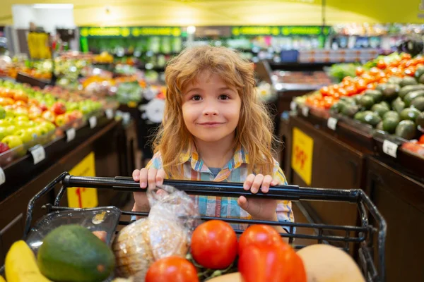 Vendita, consumismo e bambino. Ragazzino felice con cibo nel carrello della spesa al supermercato. Ragazzo si diverte mentre sceglie il cibo al supermercato. — Foto Stock