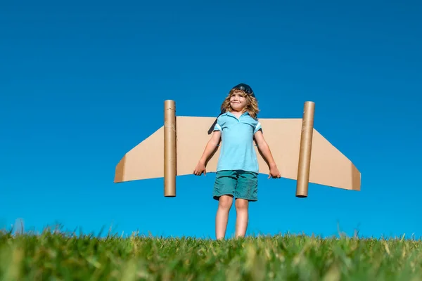 小さな子供は宇宙飛行士やパイロットを演じる。青空を背景に子供。紙の翼ジェットパックの夢を持つ子供たち。子供たちは飛ぶ夢を想像する。おもちゃのジェットパックを持つ面白い子供。成功、想像力. — ストック写真