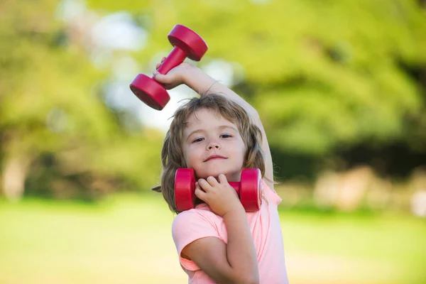 Kind jongen doet oefeningen met halters in het zomerpark. Gezonde activiteiten kids levensstijl. — Stockfoto