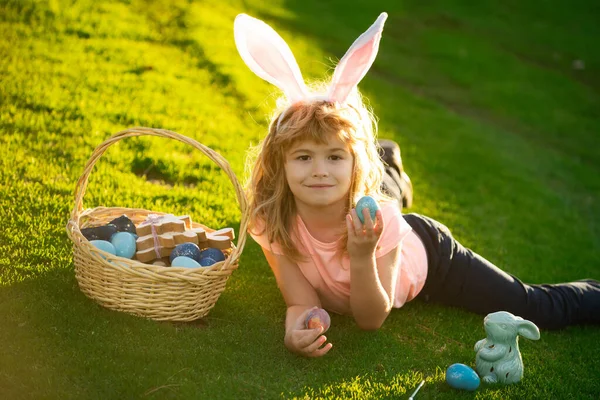 Grappige jongen, paashaas kinderen. Kind jongen met paaseieren en konijnenoren op gras. — Stockfoto