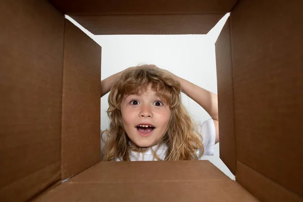 Il bambino sorpreso che disfa le valigie, apre la scatola di cartone e guarda dentro. Il pacchetto, la consegna, la sorpresa, il concetto di regalo per bambini. Scatola aperta e pacco di consegna per bambini. — Foto Stock