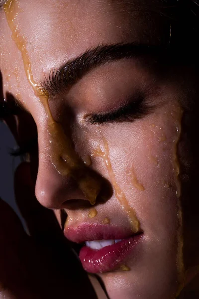 Sensual young woman face with honey drop close up. Sexy model with honey drip on face.