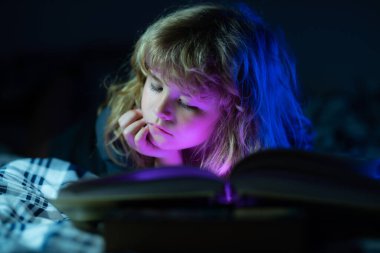 Küçük bir çocuk karanlık evde kitap okuyor. Çocukların yüzü gece lambasıyla kaplıdır. Uyku masalı, çocuk masalı..