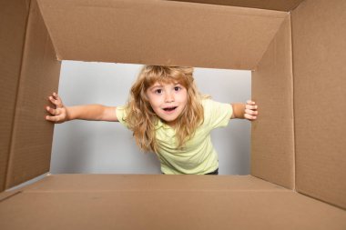 Neşeli şirin çocuk hediyesini açıyor. Karton kutular, paketler. Teslimat hizmeti konsepti. Çocuklar şaşırmış yüz ifadeleri.