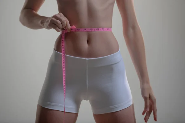 Menina magro segurando um centímetro em torno da linha da cintura. Magro jovem mulher medindo sua cintura com uma fita métrica, peso los. — Fotografia de Stock