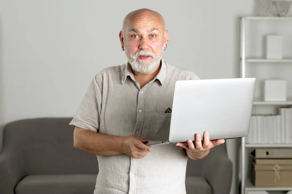 Üst düzey ofis çalışanının dizüstü bilgisayarlı portresi. Gri sakallı yaşlı adamın evde ya da ofiste bir dizüstü bilgisayarda işi var. Bilgisayar kullanan olgun bir adam. Yaşlı genel müdür.. — Stok fotoğraf