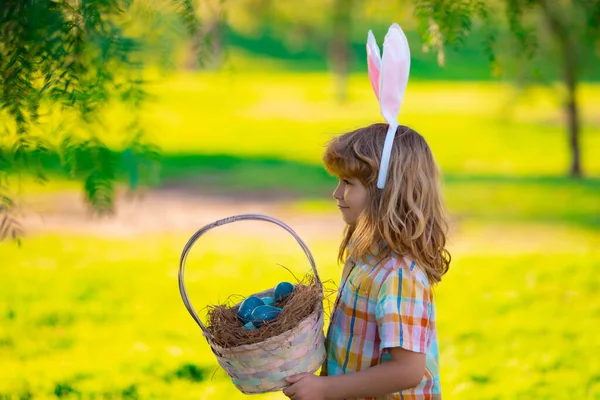 Boldog Húsvétot! Gyermek fiú nyuszi jelmezben nyuszifül vadászat húsvéti tojás a parkban. — Stock Fotó