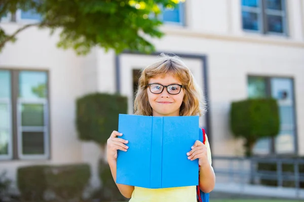 Kind aus der Grundschule. Glücklicher Junge mit Brille geht zum ersten Mal zur Schule. Kind mit Schultasche und Buch. Zurück zur Schule. — Stockfoto