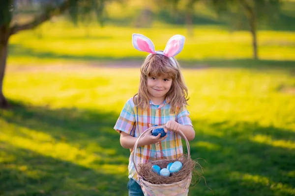 Boldog Húsvétot a gyerekeknek. A kisfiú húsvéti tojásra vadászik. Aranyos kölyök nyuszi jelmezben, nyuszifülekkel, húsvétkor a parkban. A gyerekek húsvéti tojásra vadásznak. — Stock Fotó