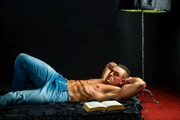 Szexi srác a hálószobában. Egy férfi az ágyban könyvvel. Szex és pihenés koncepció. Könyvimádó. — Stock Fotó