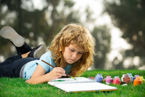 Niños escolares dibujando en el parque de verano, pintando arte. Pequeño pintor dibujar cuadros al aire libre. Niños creativos, desarrollo de la imaginación, creatividad. —  Fotos de Stock