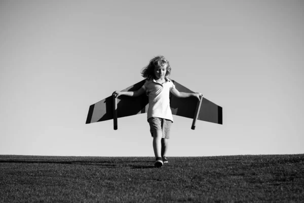 飛行機で飛ぶ子供は段ボール翼の工芸品を作った。夢、想像力、子供時代。旅行や夏休みのコンセプト。若いです男の子パイロットに対してa青い空とともにcpase. — ストック写真