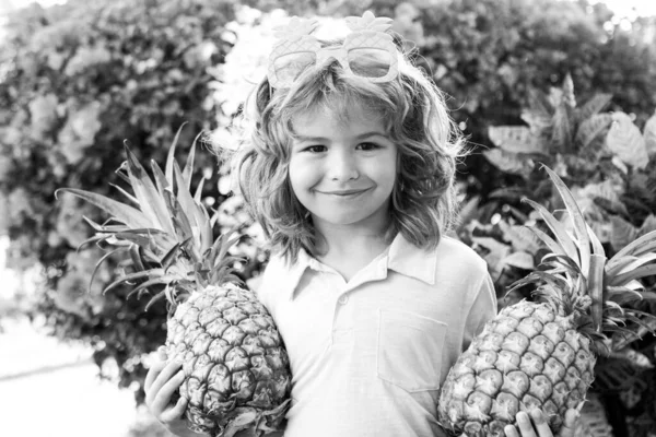 Klein blond kind knuffelt ananas op de achtergrond van de natuur. Jeugd, gezonde voeding, reclame. close-up kinderen grappig gezicht, kopiëren ruimte. — Stockfoto