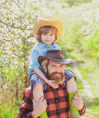 Oğlu babasının omzunda oturuyor. Bahar ailesi güneşli bir günde açık hava parkında ya da bahçede gülümsüyor..
