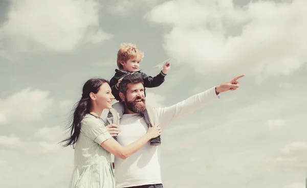 Papa, Mama und der kleine Sohn. Glückliche Familie - Sohn spielt mit Papierflugzeug. Porträt eines glücklichen Vaters, der seinem Sohn Huckepack auf den Schultern gibt, seine Frau umarmt und nach oben blickt. — Stockfoto