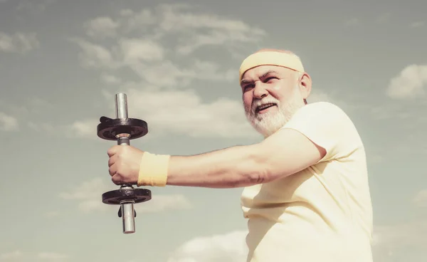 Nonno sportivo ritratto su sfondo cielo blu. Ritratto di anziano sano. Uomo anziano nei suoi anni settanta formazione e sollevamento pesare . — Foto Stock