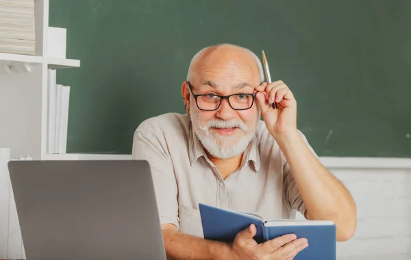 Grootvader onderwijs concept. Portret van volwassen leraar of docent professor werkzaam aan tafel op de universiteit of middelbare school. — Stockfoto