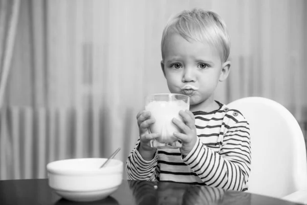 Coma saudável. A criança a comer qualquer coisa. Nutrição saudável. Bebe leite. Criança segura copo de leite. Garoto bonito menino sentar à mesa com prato e comida. Comida saudável. Menino bebê bonito tomando café da manhã. Nutrição do bebê — Fotografia de Stock