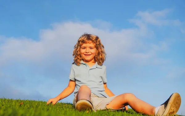Happy child boy sitting on green grass outdoors in spring park. — Stock Photo, Image