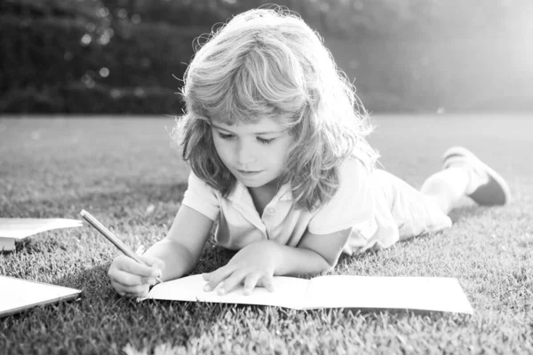 Kind ontspannen in de vakantie. Kid met potlood schrijven op notebook op gras achtergrond. — Stockfoto