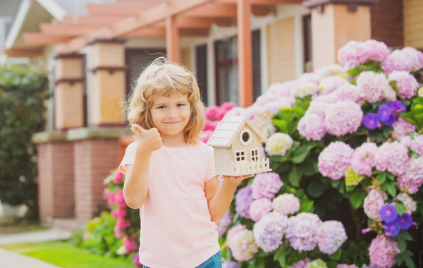 Niño con juguete pequeñas casas en manos al aire libre. Lindo niño jugando con el modelo de casa pequeña al aire libre en el jardín en casa. — Foto de Stock