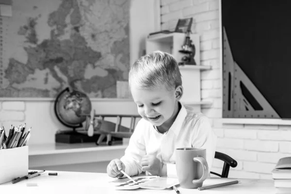 Bambino alunno è seduto a una scrivania al chiuso. Alunno carino con divertente lavoro di scolarizzazione del viso. I bambini si preparano per la scuola . — Foto Stock