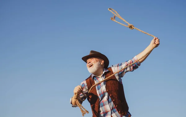 Lasso lanzando. Viejo vaquero salvaje del oeste con cuerda. Hombre occidental barbudo con chaqueta marrón y sombrero de captura de caballo o vaca. — Foto de Stock