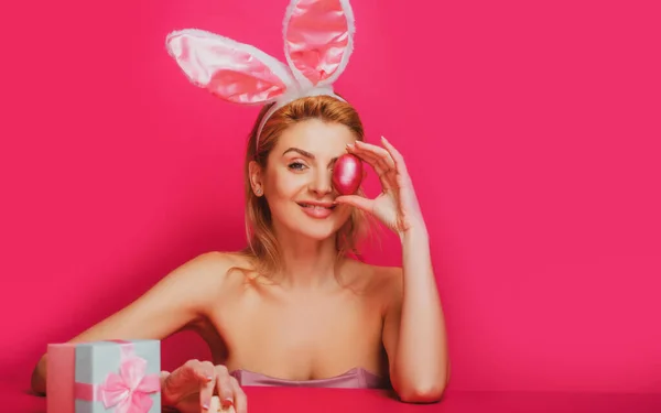 Szczęśliwej Wielkanocy. Piękna kobieta w uszach króliczka trzymająca kolorowe pisanki. Zabawna koncepcja polowania na Wielkanoc. Szczęśliwy królik model uśmiechnięty z jajkiem na twarzy odizolowany na różowy. — Zdjęcie stockowe