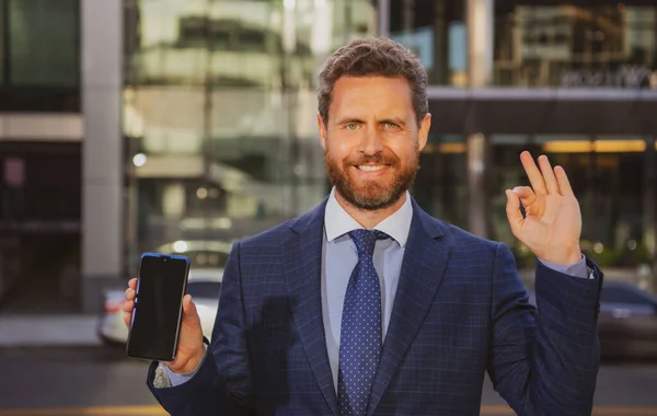 Liikemies, jolla on puhelin. Muotokuva iloinen toimistotyöntekijä puhuu matkapuhelimella seisoessaan lähellä modernia toimistoa. — kuvapankkivalokuva