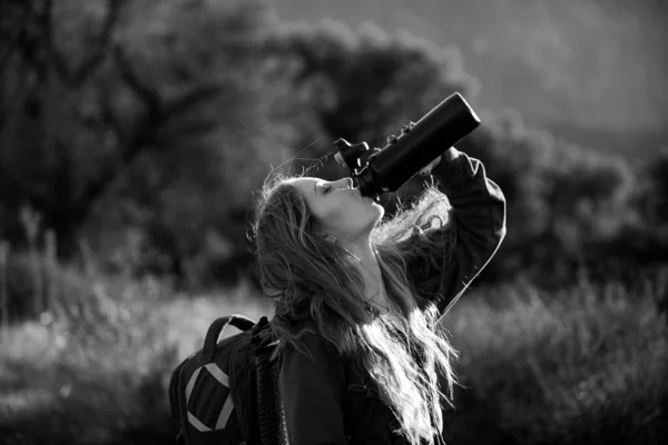 Una viaggiatrice beve acqua. Escursionista femminile con zaino in montagna. Ragazza che cammina su una collina in punto panoramico. Backpacking concetto di turismo — Foto Stock