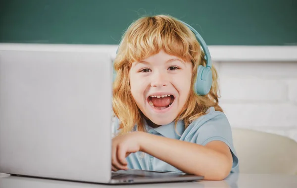 Rapaz da escola animado inteligente, aluno surpreso usa fones de ouvido escrevendo no laptop, ouvir áudio lição usar computador. — Fotografia de Stock