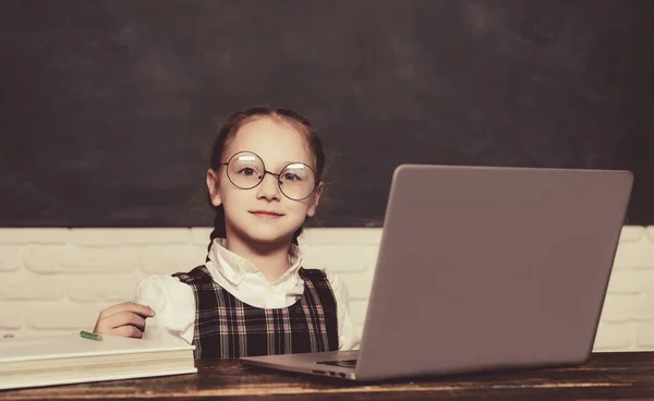 Ученица с ноутбуком. Концепция образования и чтения. Ребенок готов ответить с помощью доски на заднем плане. — стоковое фото