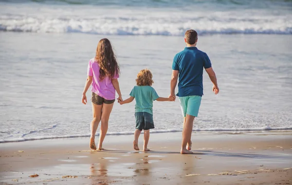 Vista posteriore di felice giovane famiglia che cammina sulla spiaggia. Bambino con genitori che si tengono per mano. Popolo a tutta lunghezza. Viaggi in famiglia, concetto di vacanza. — Foto Stock