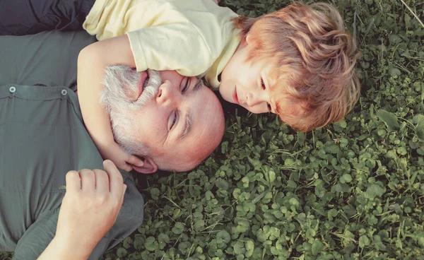 Abrazo y abrazo en la hierba verde - abuelo y nieto. Feliz hombre mayor Abuelo con lindo nieto niño jugando en el parque. — Foto de Stock