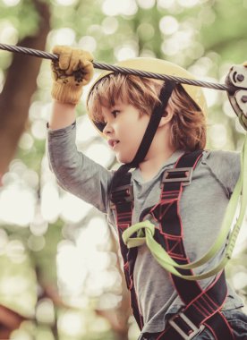 Ağaç evde ya da halat parkında güvenlik ekipmanlarına tırmanan sevimli bir çocuk ipe tırmanıyor. Mutlu küçük çocuk halatla oyun sahasına tırmanıyor..