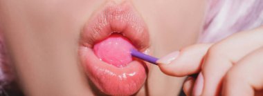 Dudak yalayıcı pankart. Ağzında kırmızı lolipop şekeri tutan pembe rujlu yakın plan kadın dudakları. Oral seks konsepti. Yüzünde lolipop var..