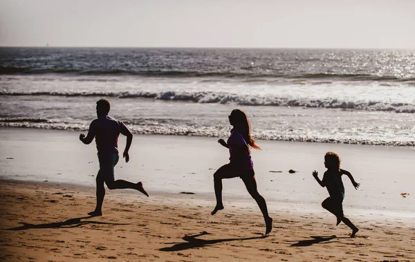 砂浜を走るフィットネスファミリー。スポーティ家族の父、母親と赤ちゃんの息子が一緒に実行されます。海に沿って水で動く親を持つ子供。スポーツ、夏の健康。健康的なライフスタイル. — ストック写真
