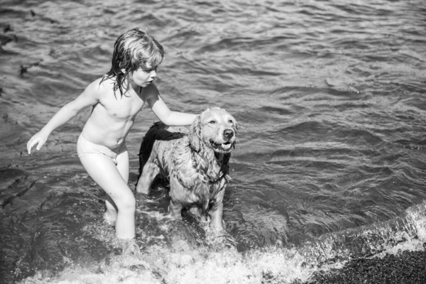 Счастливый ребенок играет с собакой на пляже. Мальчик играет с собакой в воде. — стоковое фото