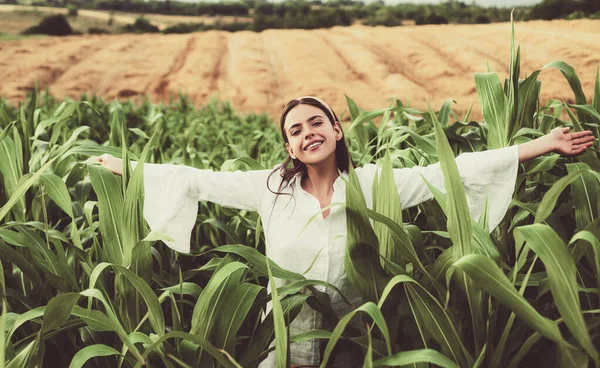 Femme fermière joyeuse posant dans la récolte de maïs. Jeune fille heureuse montrant le maïs récolté dans le champ. — Photo