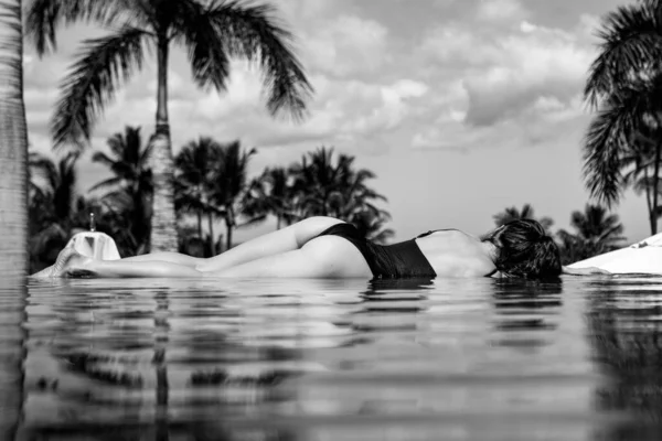 Egy nő a végtelen medencében. Fiatal lány élvezi a napsütést a medence mellett. Nyaralás, nyaralás, napozás, utazás pihenés koncepció. Nyári szabadidő, egészséges aktív életmód. — Stock Fotó