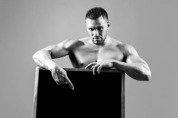 Fitness muž s reklamní tabulí. Silný kulturista macho držení prázdný plakát izolované na šedém pozadí. — Stock fotografie