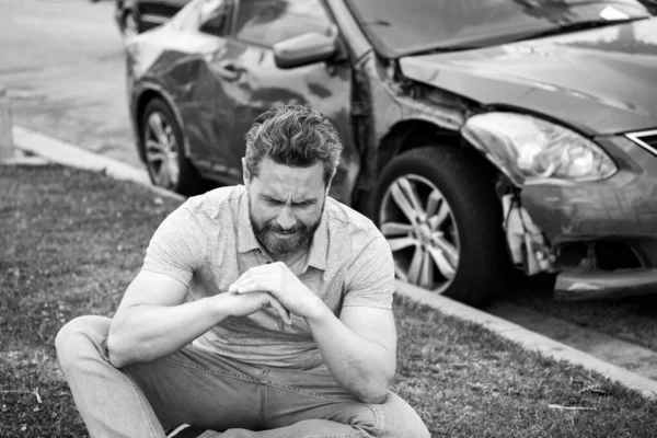 Αναστατωμένος οδηγός κάθεται στο δρόμο δίπλα στο σπασμένο αυτοκίνητο. — Φωτογραφία Αρχείου