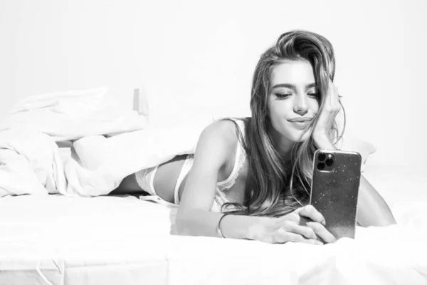 Woman in bed checking social apps with smartphone. Sexy girl making video call, lying on bed in the morning. — Stock Photo, Image